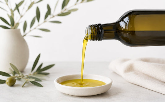 Extra virgin olive oil being poured into a bowl with olive branches in the background.