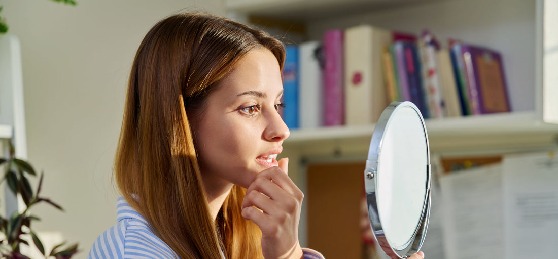 a concerned young woman looking at her face in a mirror
