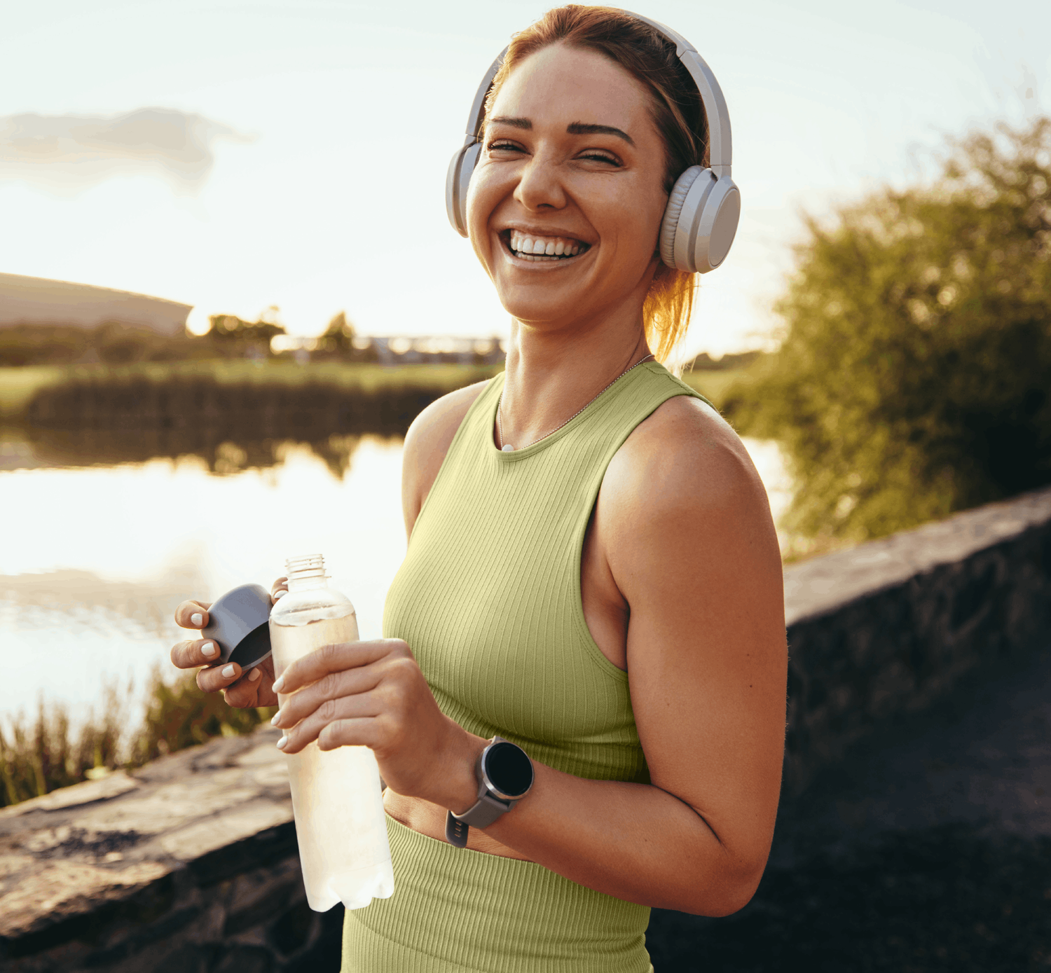 Woman outdoors after exercise, holding a water bottle and smiling by a lake.